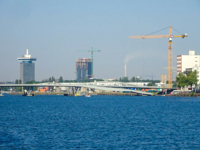 City skyline with bridge and cranes over blue water.